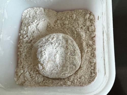 Covering a paratha dough ball with flour.