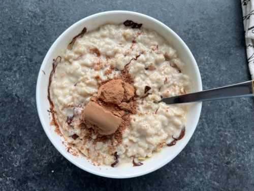 A white bowl with a spoon filled with peanut butter oatmeal and topped with cocoa powder before mixing.