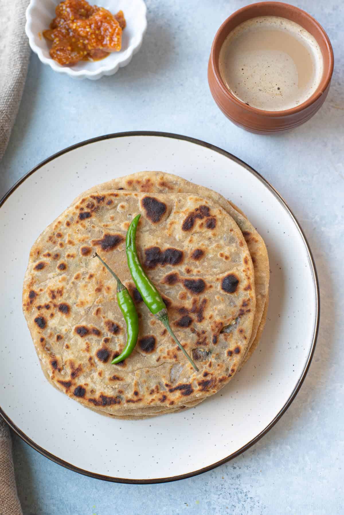 A stack of onion parathas topped with chilies.