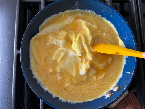 A yellow spatula scrambling the eggs in the non-stick pan.