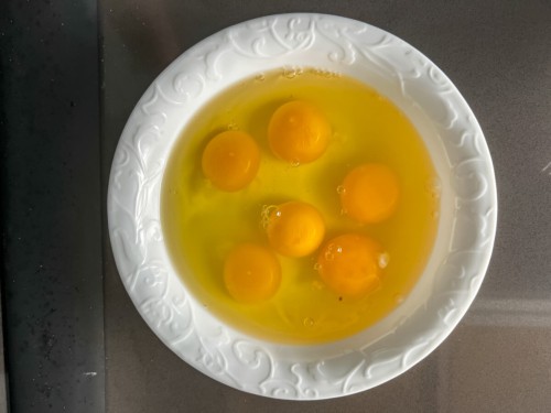 A white rimmed bowl with eggs before whisking.