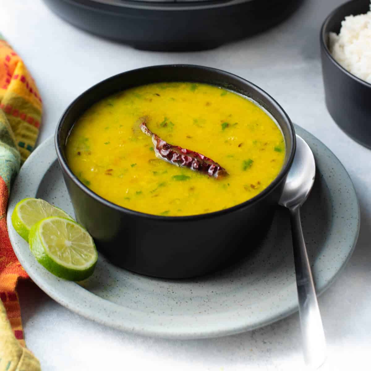 Dal served in a black bowl kept on a grey plate with lime slices 