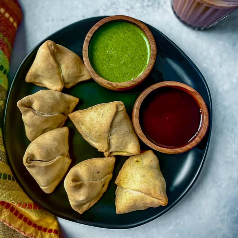 A plate with samosas and a variety of sauces for serving.
