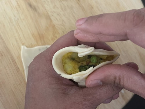 Pressing together a samosa cone to seal the edges.