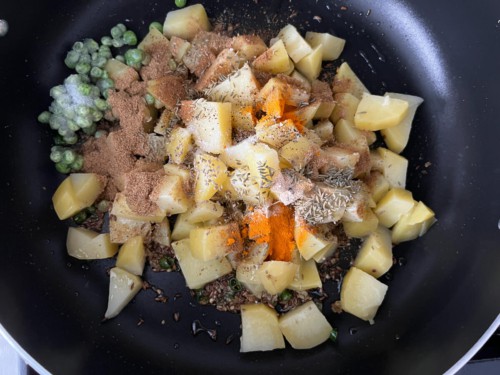 Adding potatoes, peas, and spices to a wok.