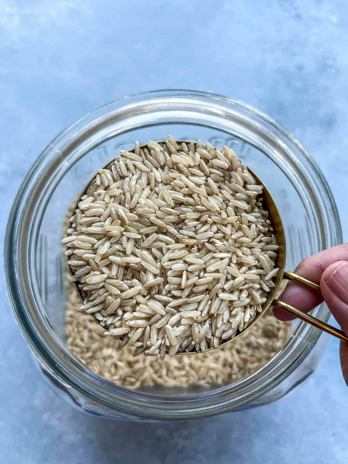 Scooping a cup of brown rice from a jar.