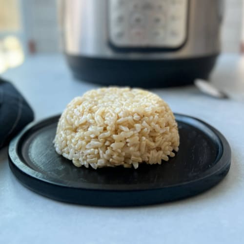 A form of brown rice on a black plate, with an Instant Pot in the background.