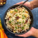 Hands holding a bowl of basmati rice with garnish.