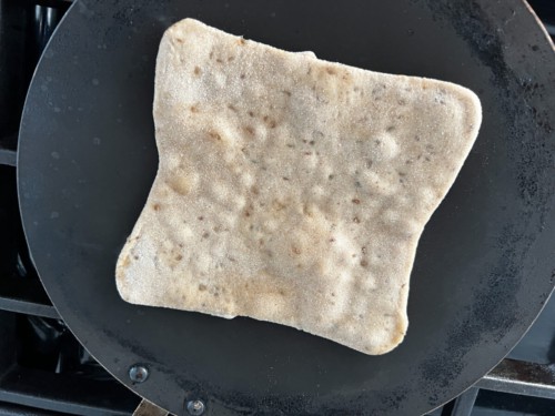 The paratha is placed in a hot pan to cook. Bubble within the dough are starting to appear.