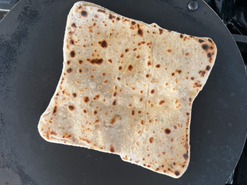 Cooking the paratha in a hot pan. It is white with a couple of dark spots appearing.