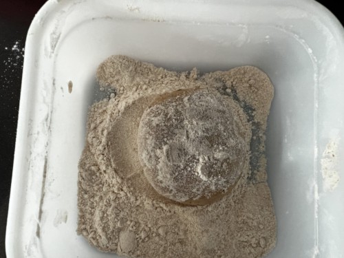 A ball of dough has been placed into a tub containing flour mixture and coated.