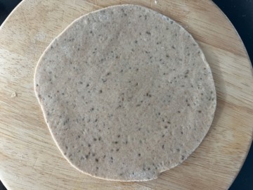 The paratha dough on a wooden surface is in a circle shape.