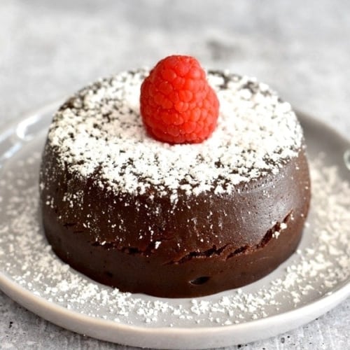 Chocolate lava cake placed on a grey plate sprinkled with powdered sugar and topped with a raspberry