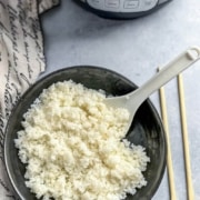 Sushi rice in a black bowl with rice paddle, Instant Pot in background.