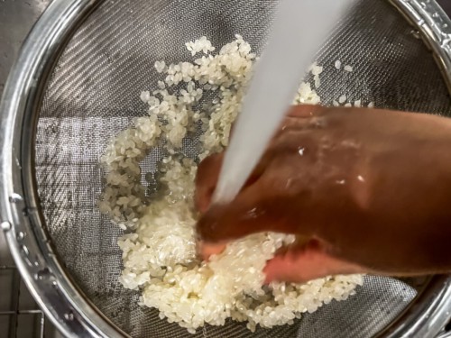Hand rinsing grains in a colander under running water.