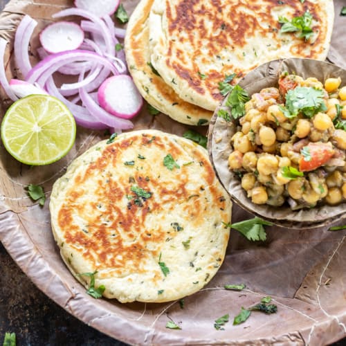 Bread kulcha served in a brown plate with a pea curry with lime slices and onions