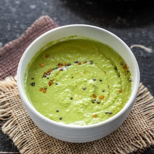 Cilantro coconut chutney served in a white bowl kept over burlap squares