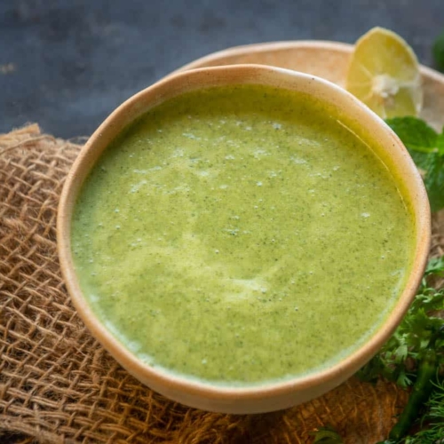 Green dahi chutney served with a cream bowl with lemon slices and mint