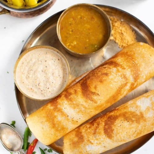Two dosa served in a brass plate with coconut chutney and sambar