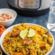White bowl with paneer biryani, topped with two slices of lime.