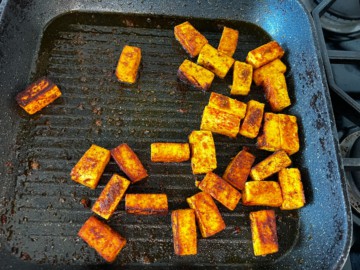 Pieces of paneer cooked on a grill plate.