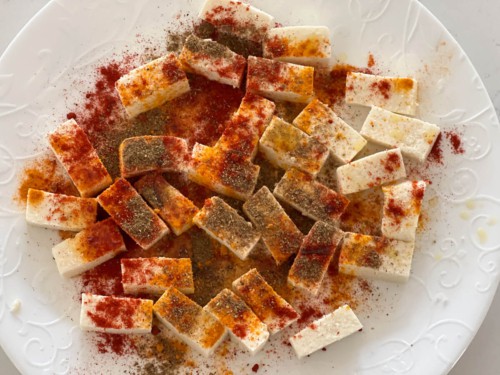 Cubes of paneer on a white board, coated with spices.