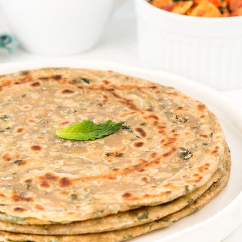 Mint paratha served on a white plate with pickle on the side