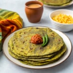 Stack of palak parathas on a white plate with dollop of chili sauce on top.