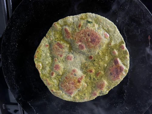 Palak paratha on skillet flipped a second time to cook on other side.
