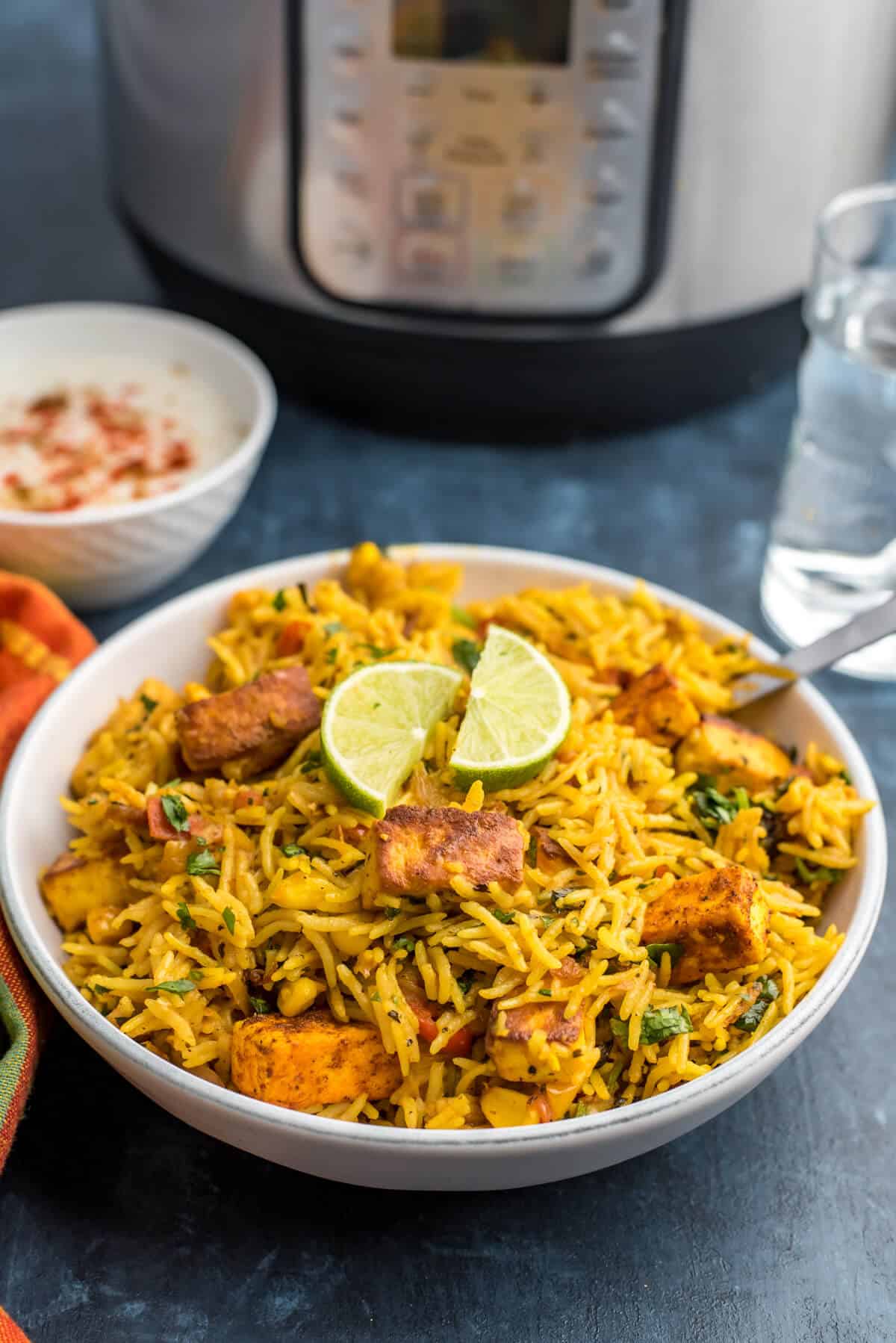 White bowl with paneer biryani, topped with two slices of lime.