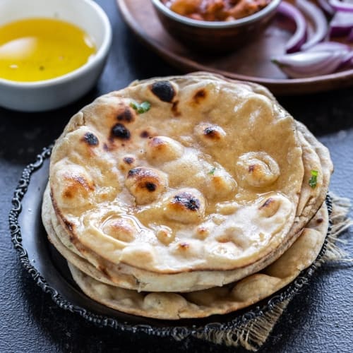 Butter laden Tandoori roti stacked on a black plate 