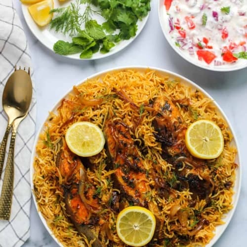 Fish biryani served in a white bowl topped with lemon slices