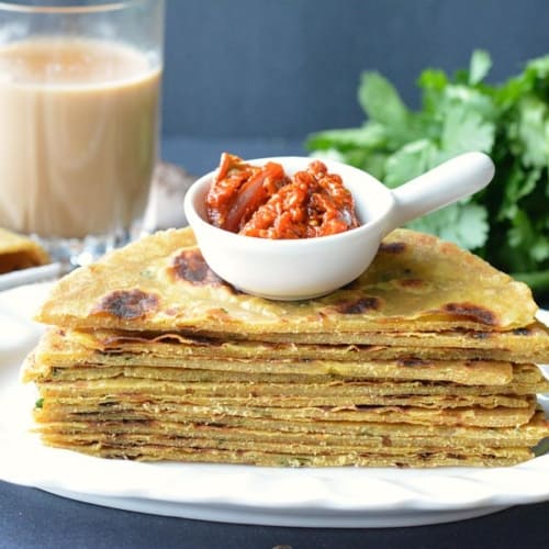 Parathas stacked in a white plate with a white bowl of pickle kept on top