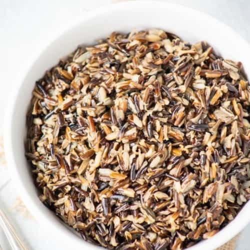 Wild rice served in a white bowl with spoons on the side