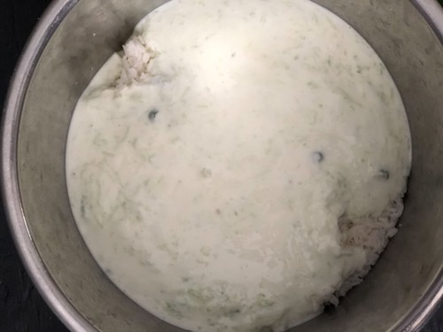 Yogurt-milk mixture added to rice in a steel bowl for making curd rice
