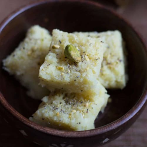 4 pieces of coconut barfi stacked in a brown bowl