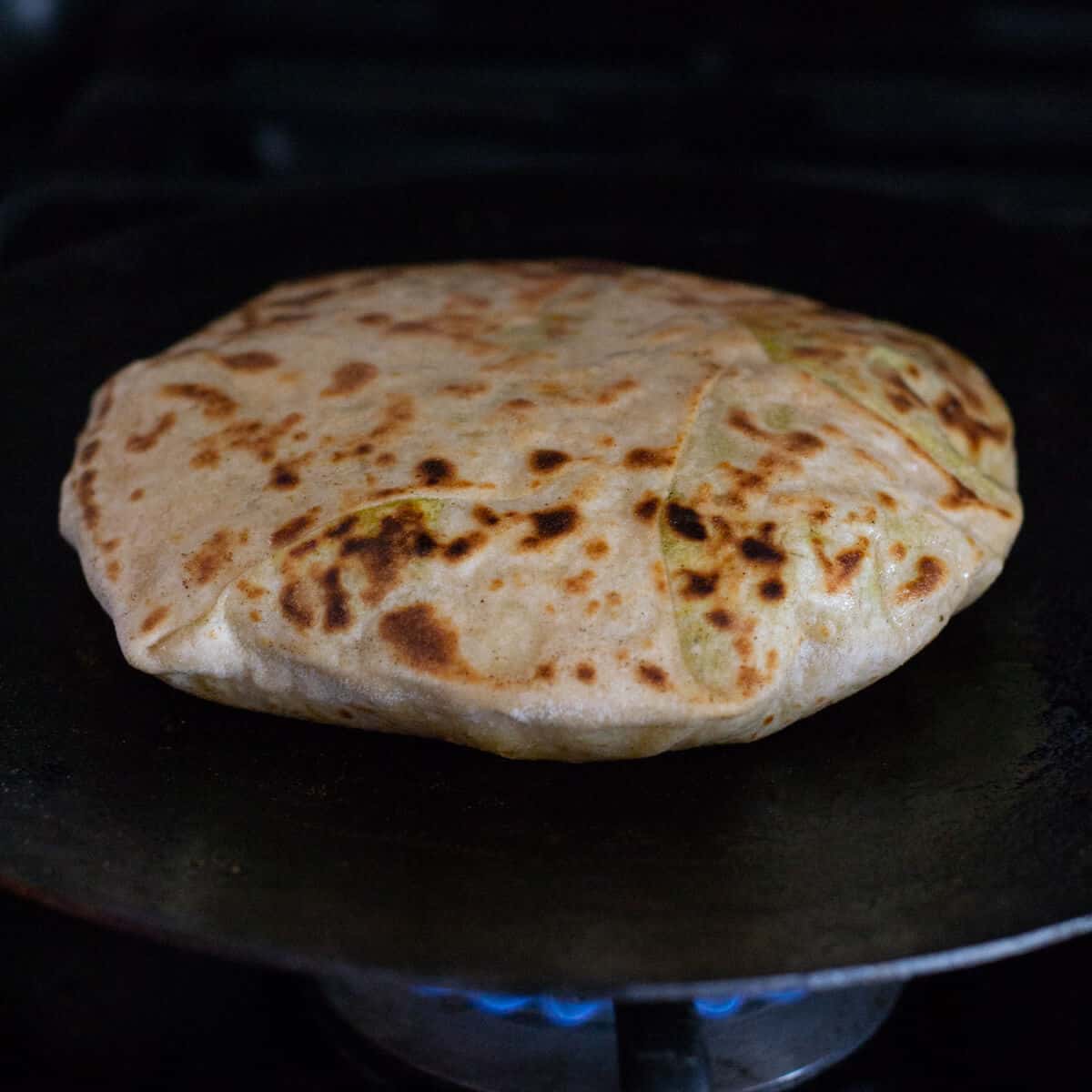 Puffed up Aloo paratha in a pan over gas